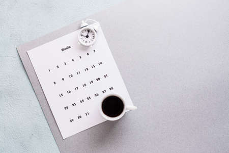 Blank sheet of monthly calendar, coffee cup and alarm clock on textured background. Time planning and organization. Copy spaceの写真素材