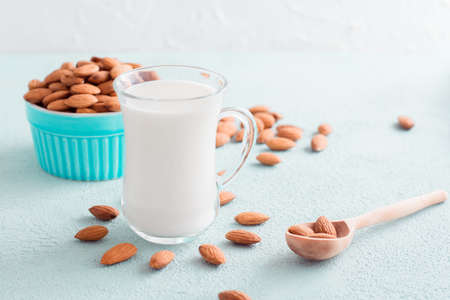 Fresh almond milk in a glass and almonds in a wooden spoon on a light background. Alternative nutrition, source of vitaminsの写真素材
