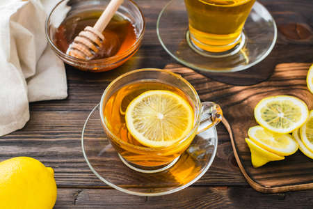 A cup of tea with a slice of lemon and a bowl of honey on a wooden table. Vitamin warm drink....