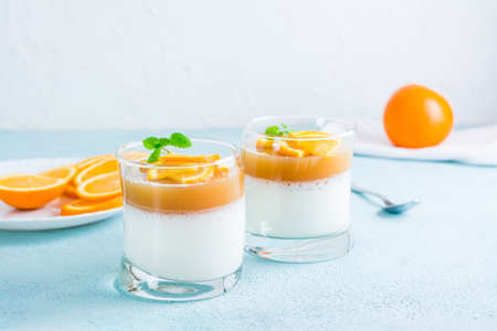 Panna cotta with orange and mint leaf in glasses on a light table. Sweet Italian dessertの写真素材