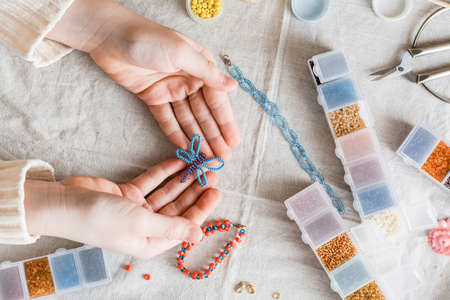 A beaded butterfly in the hands of a girl and items for beadwork on the table. Development of creative skills and fine motor skills for children. top view.の写真素材