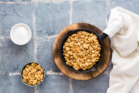 Fresh roasted peanuts in a frying pan, salt and oil on the table. Plant source of protein....
