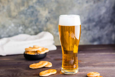 Glass of beer with foam and salty pretzels on a wooden table