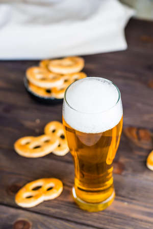 Glass of beer with foam and salty pretzels on a wooden table. vertical view. close-upの写真素材