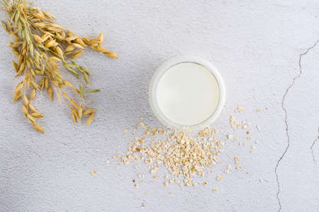 Oat milk in a glass, ears and scattered dry oatmeal on a light table. Alternative plant food. top...
