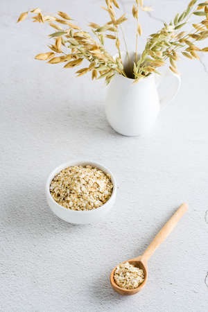 Dry oatmeal in a bowl and in a wooden spoon and a jug with ears on a light table. home healthy food....