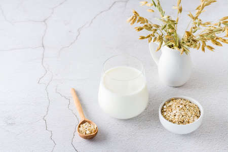 Oat milk in a glass, oatmeal in a bowl and ears in a jug on a light table. Alternative plant food. copy spaceの写真素材