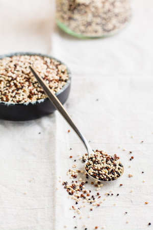 Mix of raw white, red and black quinoa in a bowl and in a spoon on a cloth. Healthy gluten free food. vertical viewの写真素材