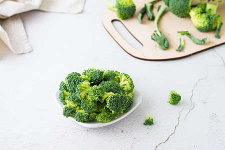 Pieces of raw broccoli on a plate on a light table. Cooking healthy vegetarian food. copy space
