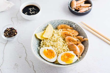 Chinese noodles with fried shrimp, boiled egg and lemon in a bowl on the table. Asian food. close-upの写真素材