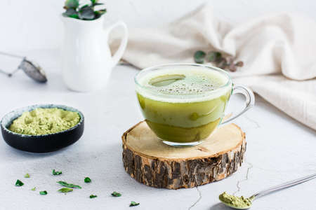 Organic green matcha tea in a cup on a tree trunk on the table. Source of vitamins and antioxidants