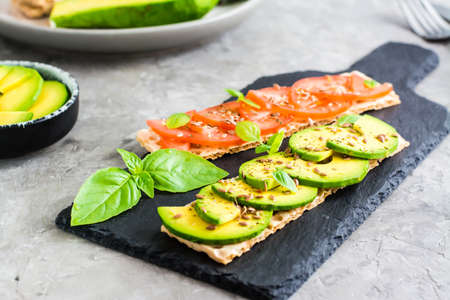Appetizing sandwiches with avocado and tomatoes on grain bread on slate on the table. Vegetarian...