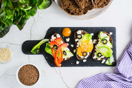 Appetizing bruschetta with feta cheese and vegetables on rye bread on a slate board. Healthy diet food. top viewの写真素材
