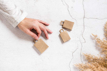A woman's hand holds paper craft shopping bags on a concrete background. Sustainable lifestyle,...