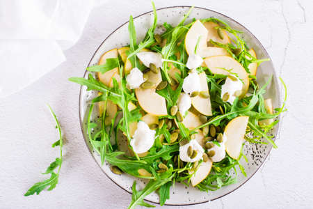 Pear salad with arugula, cheese and pumpkin seeds on a plate on the table. Homemade vitamin lunch. top view. close-upの写真素材