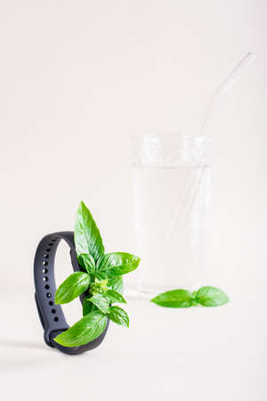 Fresh leaves on the screen of a fitness bracelet and a glass of water. The concept of health care, vitality. vertical viewの写真素材