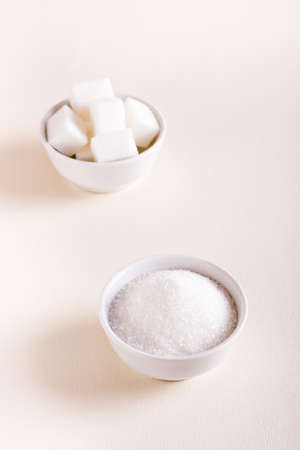 Granulated sugar and sugar cubes in bowls on a pink background. Choosing between types of sugar. vertical viewの写真素材