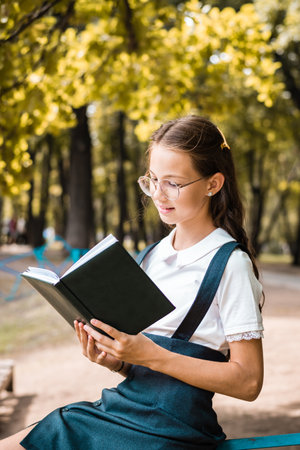 Schoolgirl with glasses reading a book on a warm day in the park. vertical viewの写真素材