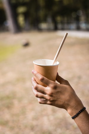 Disposable paper cup with a drinking straw in the hand of a teenager in the park on a warm dayの写真素材