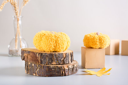 autumn decoration. Knitted pumpkins on a cut of a tree and on a cube on a light backgroundの写真素材