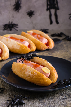 An amputated sausage finger in ketchup in a bun on a plate. Halloween recipe. vertical viewの写真素材