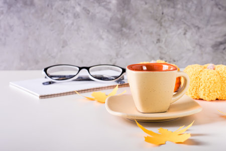 Cup of black coffee, notebook, glasses, paper maple leaves and knitted pumpkins on the tableの写真素材