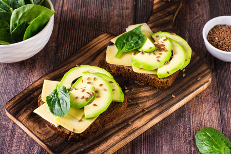 Rye bread bruschetta with avocado, cheese, spinach and flax seeds on a board on the table. Health...