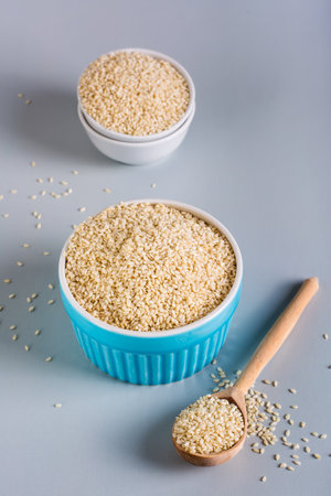 Sesame seeds in bowls and in a wooden spoon on a gray background. organic food. vertical viewの写真素材