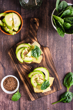Rye bread bruschetta with avocado, cheese, spinach and flax seeds on a board on the table. Health food. Top and vertical viewの写真素材