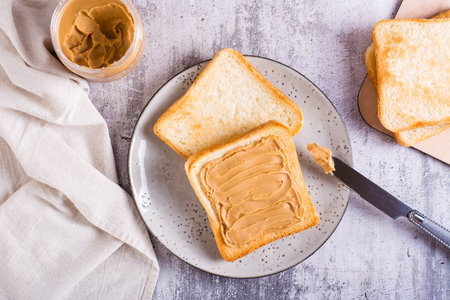 Peanut butter sandwich on toasted bread on a plate and jar of butter on the table. top view