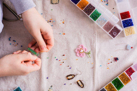 Children's hands weave a beaded toy on a table among boxes with beads. top viewの写真素材