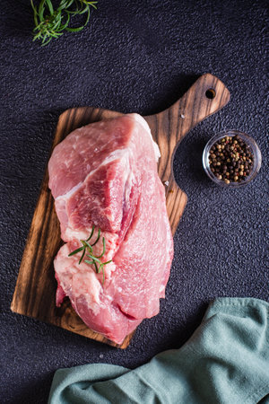 Large piece of pork, rosemary and salt on a cutting board on a black background. Top and vertical viewの写真素材