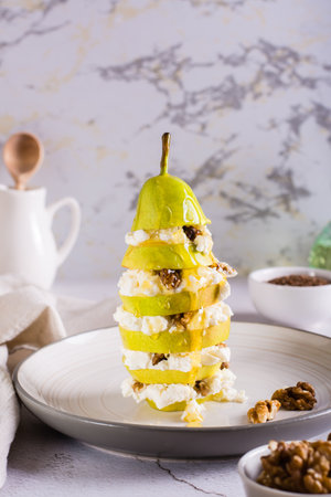 Pear with ricotta, honey and walnuts in layers on a plate on the table. Health food. vertical viewの写真素材