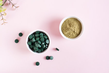 Detox products. Spirulina seaweed in pills and matcha tea powder in bowls on a pink background. top viewの写真素材