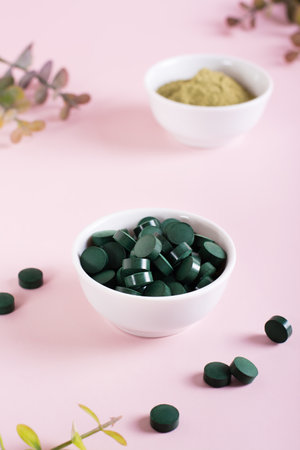 Detox products. Spirulina seaweed in pills and matcha tea powder in bowls on a pink background. vertical viewの写真素材