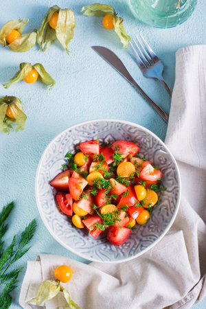 Appetizing salad with physalis, tomatoes and dill in a bowl. Vegetarian diet. Top and vertical viewの写真素材