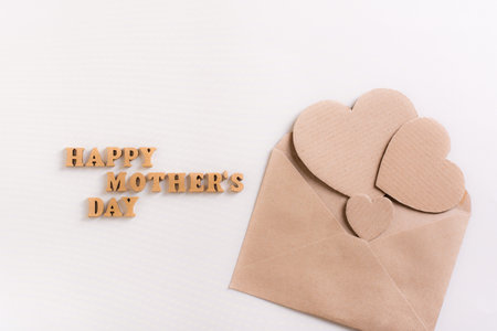 Happy mother's day. Wooden letters and cardboard hearts in an envelope on a light background.