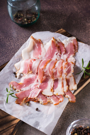 Raw bacon slices on paper on a cutting board on the table. Hearty snack. vertical viewの写真素材