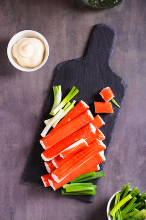 Spicy crab sticks and green onions on a stone board and sauce in a bowl on the table. Top and vertical viewの写真素材