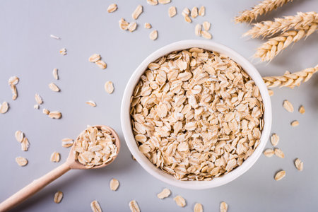 Close-up raw oatmeal in a bowl with a wooden spoon and ears on a gray background. top viewの写真素材