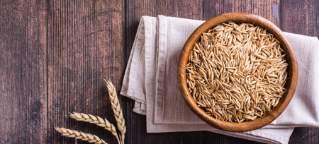 A plate with unpeeled oat seeds and ears of oats on a wooden table. top view. web bannerの写真素材