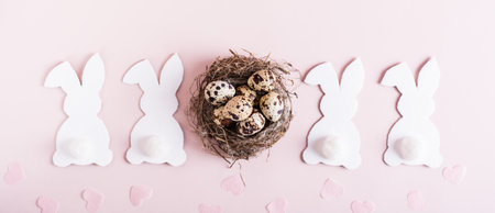 Web banner happy easter white cardboard rabbits, nest with eggs and hearts on pink background top viewの写真素材