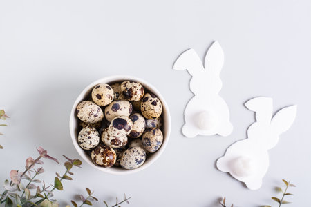 A pair of white rabbits and a bowl of quail eggs on a gray background for a happy easter top view