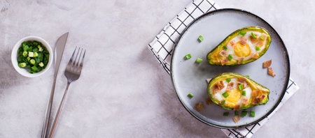Egg baked in avocado sprinkled with bacon and herbs on a plate top view web bannerの写真素材