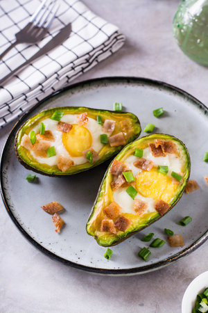 Egg baked in avocado sprinkled with bacon and herbs on a plate vertical viewの写真素材