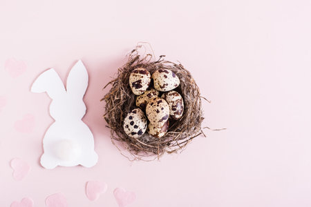 Happy easter nest with quail eggs and white cardboard rabbit on pink background top viewの写真素材