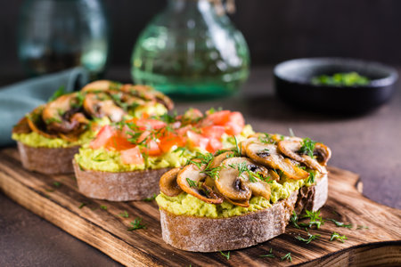 Sandwiches with avocado, fried champignons, tomatoes and herbs on rye bread on a boardの写真素材