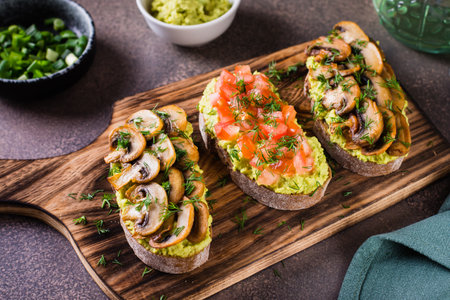 Sandwiches on rye bread with guacamole, fried mushrooms, tomatoes and dill on a boardの写真素材
