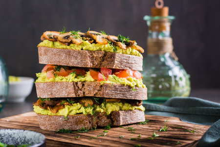 Close-up of a layered rye bread sandwich with guacamole, fried mushrooms, tomatoes and dillの写真素材