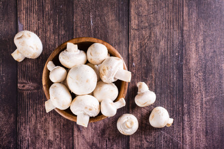 Raw whole champignons in a bowl and on a wooden table top viewの写真素材